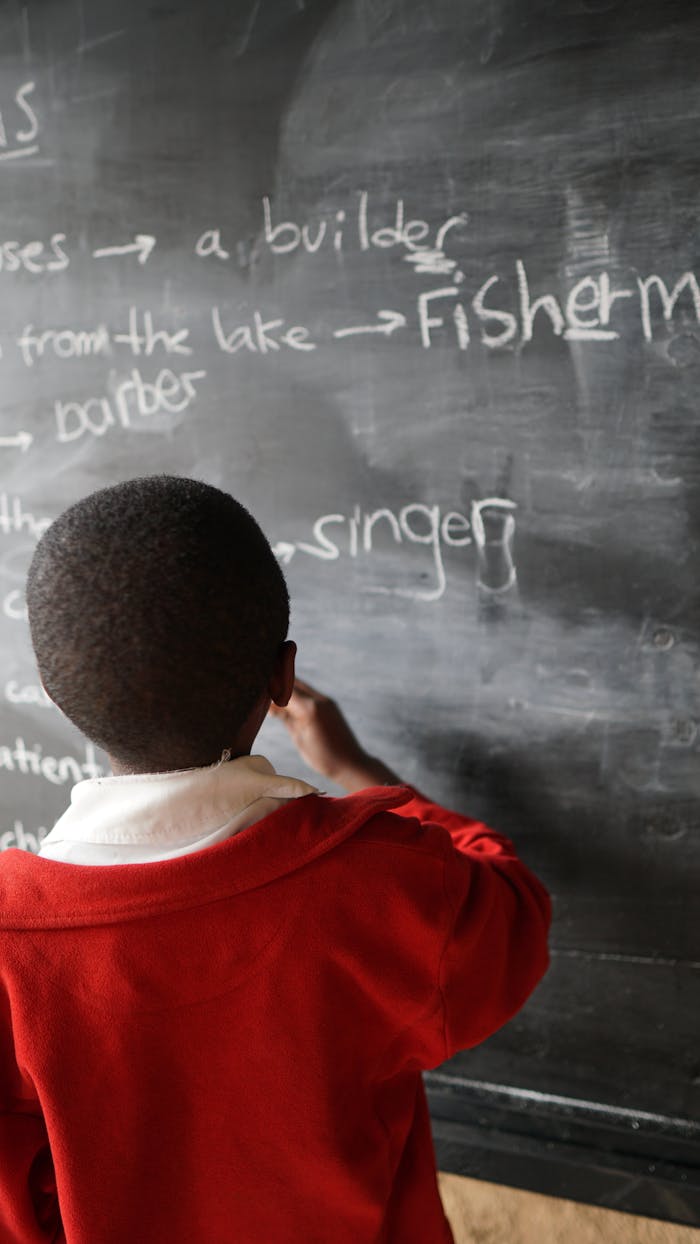 Young student in a red uniform writing on a blackboard, focusing on education and learning.